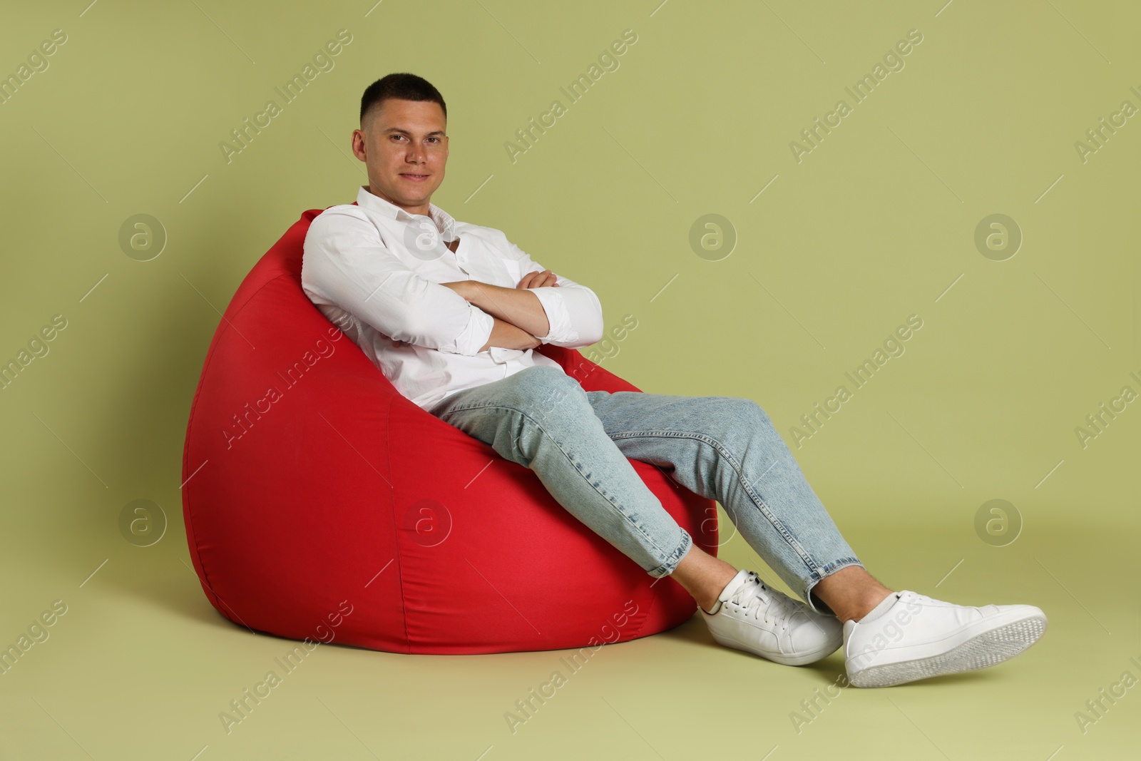 Photo of Handsome man with crossed arms on red bean bag chair against green background