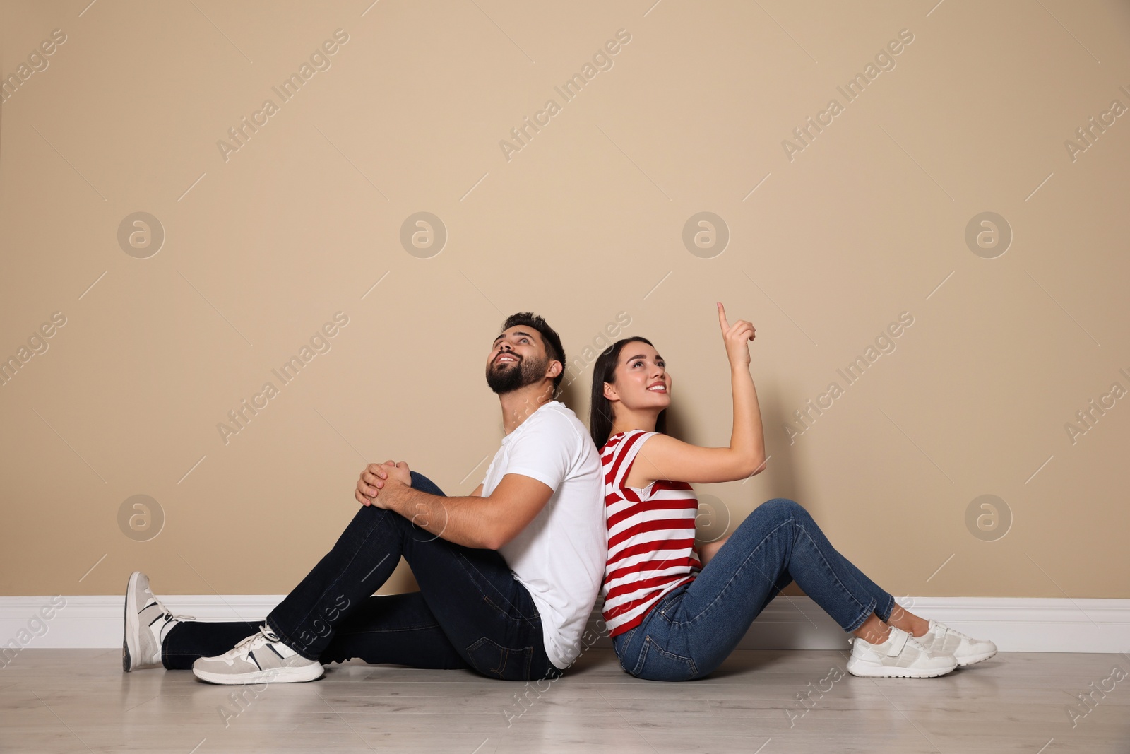 Photo of Young couple sitting on floor near beige wall indoors