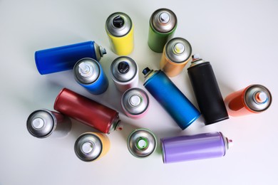 Photo of Cans of different graffiti spray paints on white table, flat lay