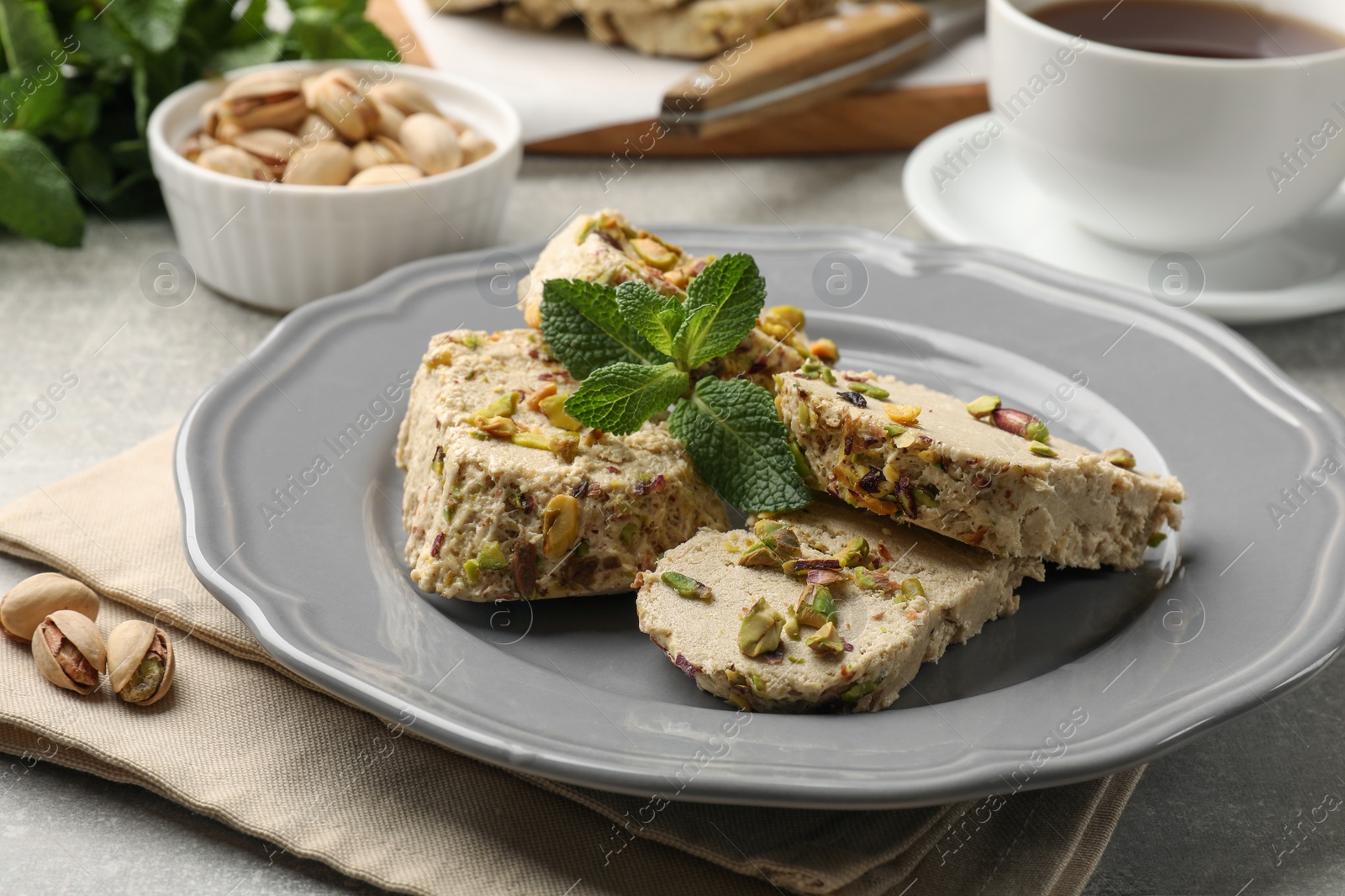 Photo of Tasty halva with pistachios and mint served on light grey table, closeup