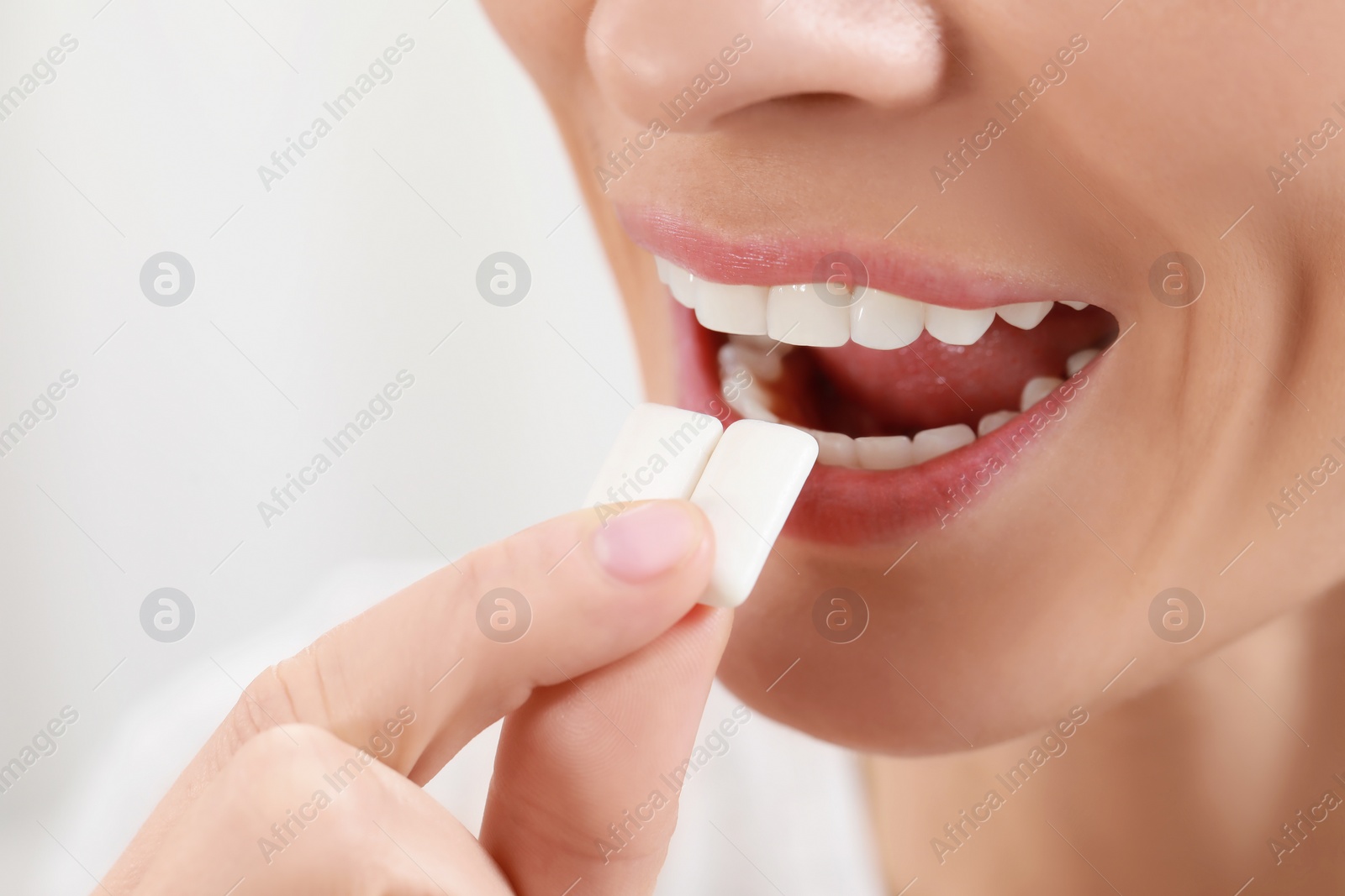Photo of Woman putting chewing gum pieces into mouth on blurred background, closeup