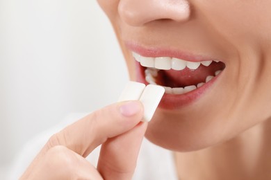 Photo of Woman putting chewing gum pieces into mouth on blurred background, closeup