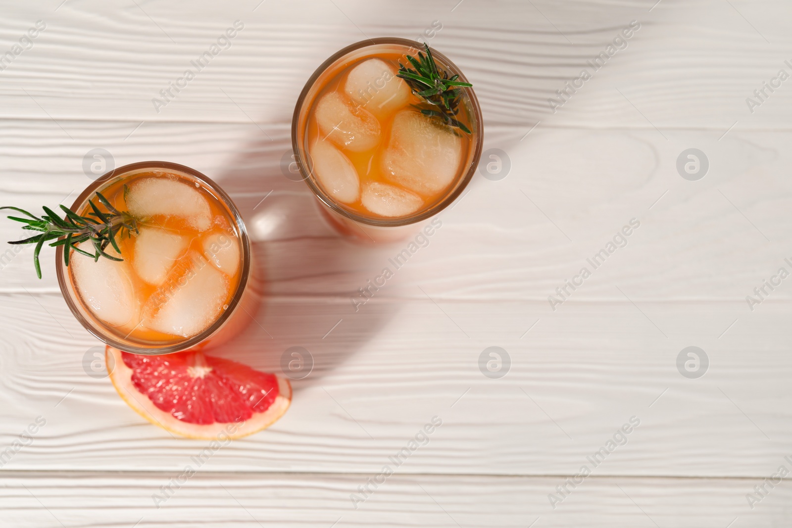 Photo of Tasty grapefruit drink with ice and rosemary in glasses on white wooden table, top view. Space for text