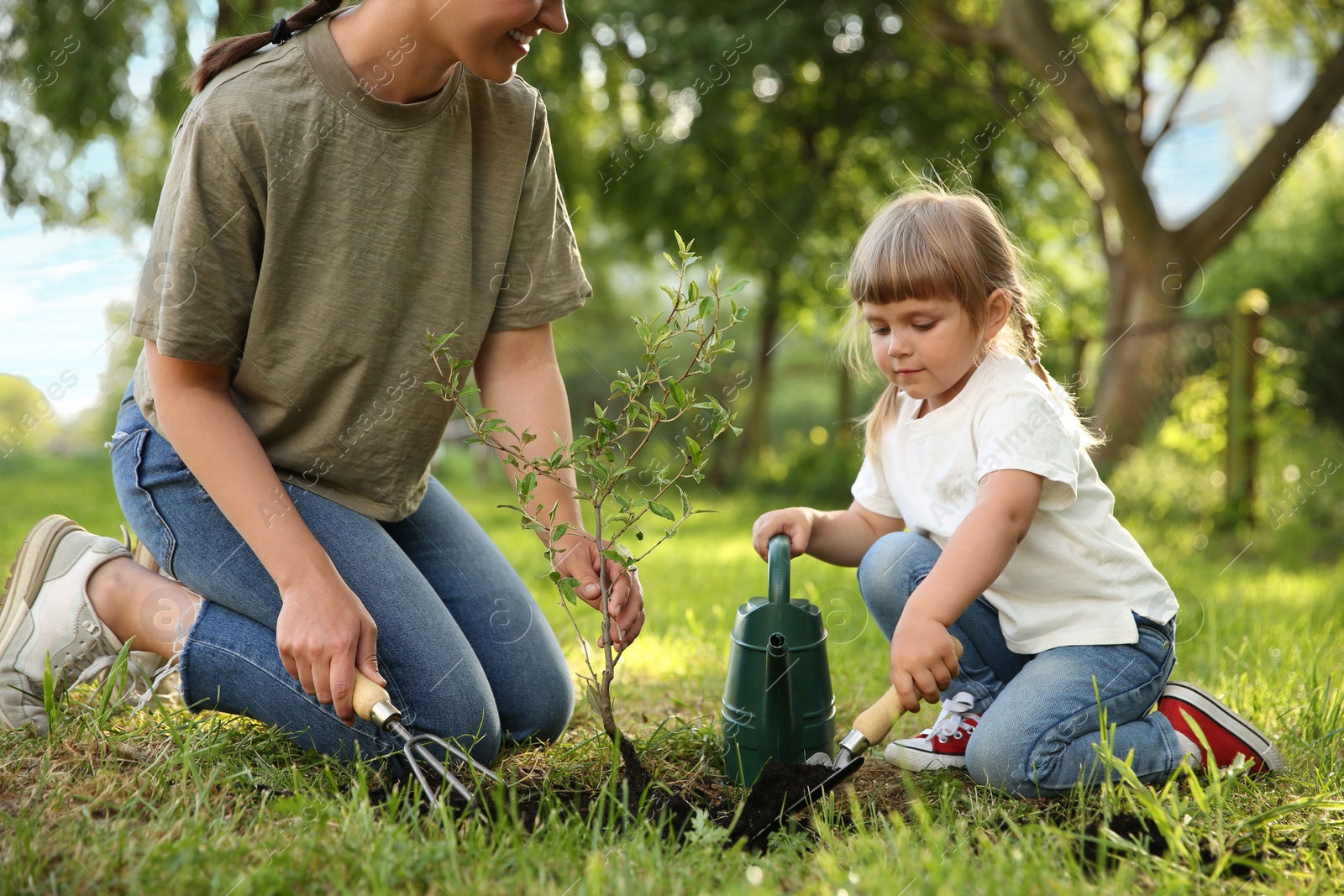 Photo of Mother and her daughter planting tree together in garden