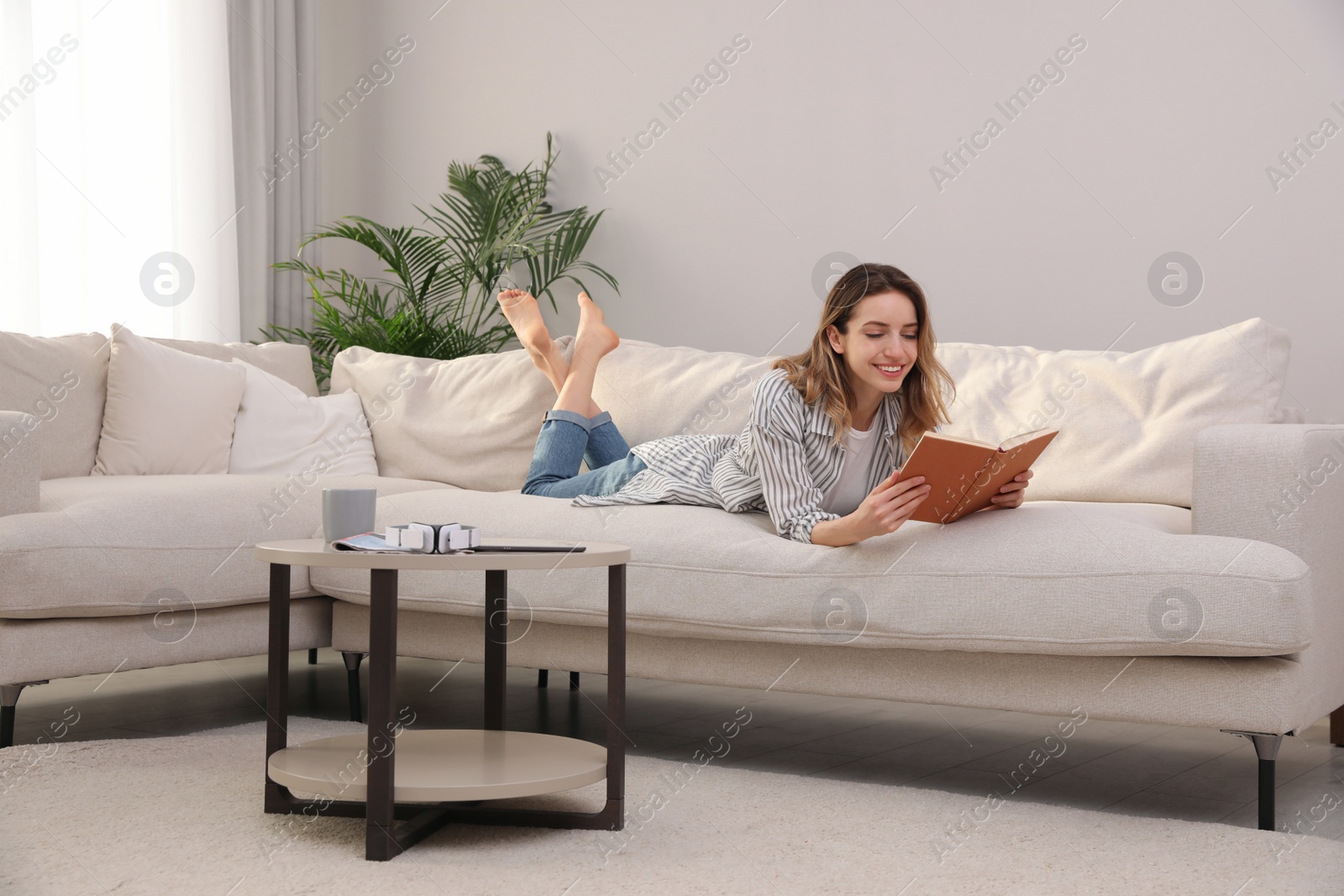 Photo of Young woman reading book on sofa at home