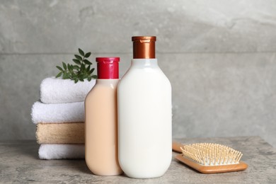 Photo of Bottlesshampoo, hairbrush and stacked towels on grey table