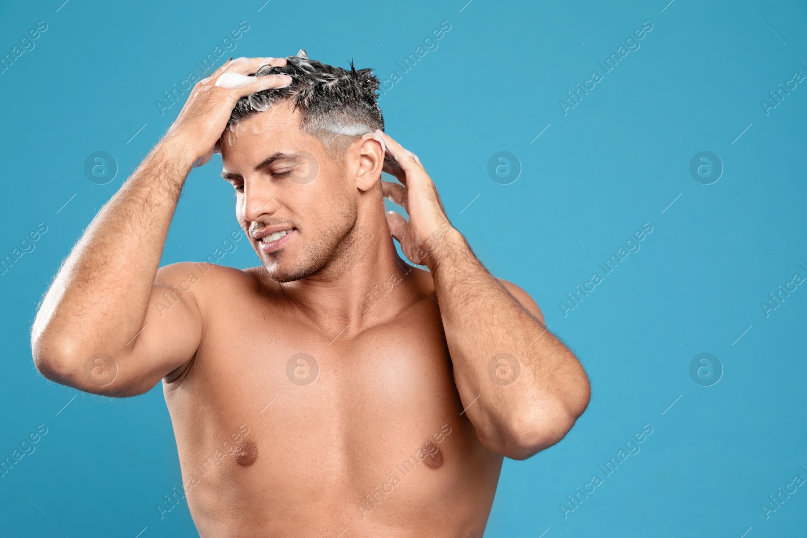 Photo of Handsome man washing hair on light blue background