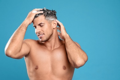 Handsome man washing hair on light blue background