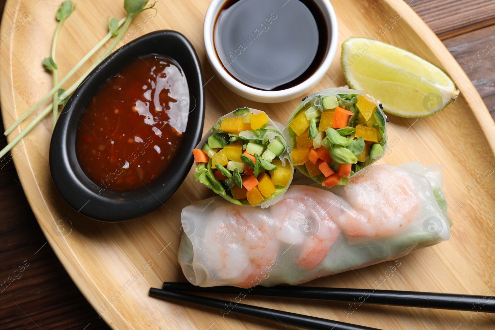 Photo of Tasty spring rolls and sauces on wooden table, top view