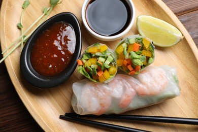 Photo of Tasty spring rolls and sauces on wooden table, top view