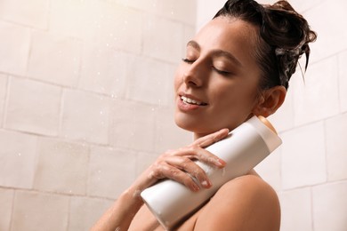 Happy woman with bottle of shampoo in shower at home, space for text. Washing hair