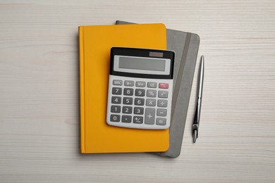 Calculator, notebooks and pen on white wooden table, flat lay