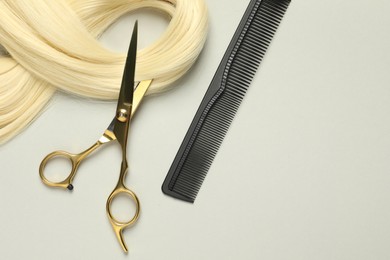 Professional hairdresser scissors and comb with blonde hair strand on light grey background, flat lay. Space for text