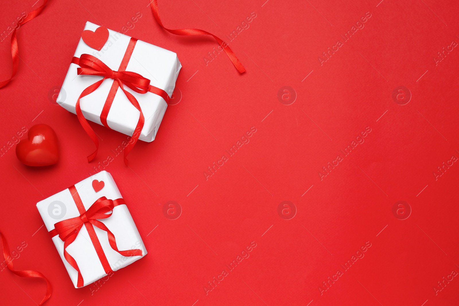 Photo of Beautiful gift boxes and decorative heart on red background, flat lay. Space for text