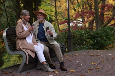 Photo of Affectionate senior couple with cups of coffee spending time together on bench in autumn park, space for text