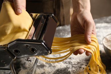 Woman preparing noodles with pasta maker machine at table, closeup