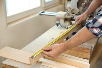 Working man measuring timber strip in carpentry shop, closeup