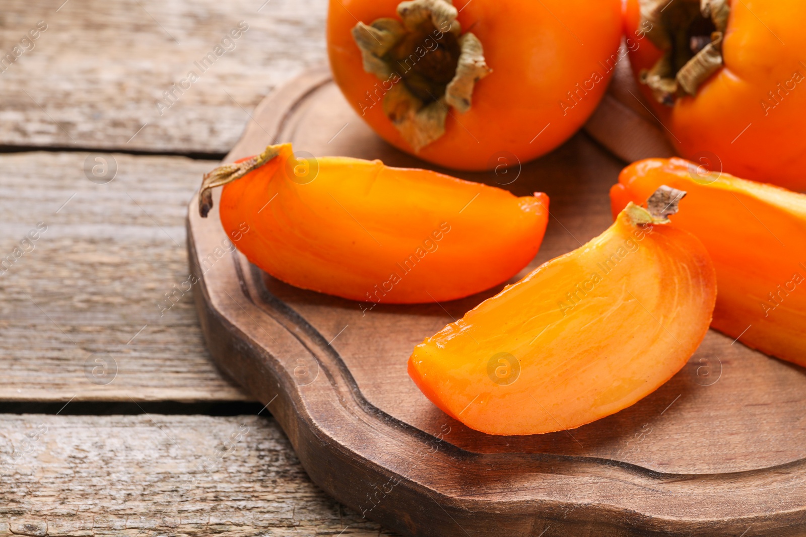 Photo of Whole and cut delicious ripe persimmons on wooden table, closeup. Space for text