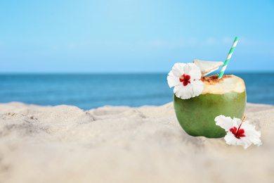 Image of Green coconut with refreshing drink and flowers on sandy beach near sea, space for text