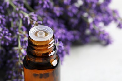 Bottle with essential oil near lavender on table, closeup. Space for text