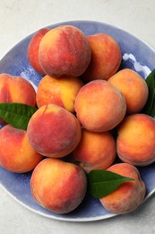 Photo of Many whole fresh ripe peaches and green leaves in plate on white table, top view