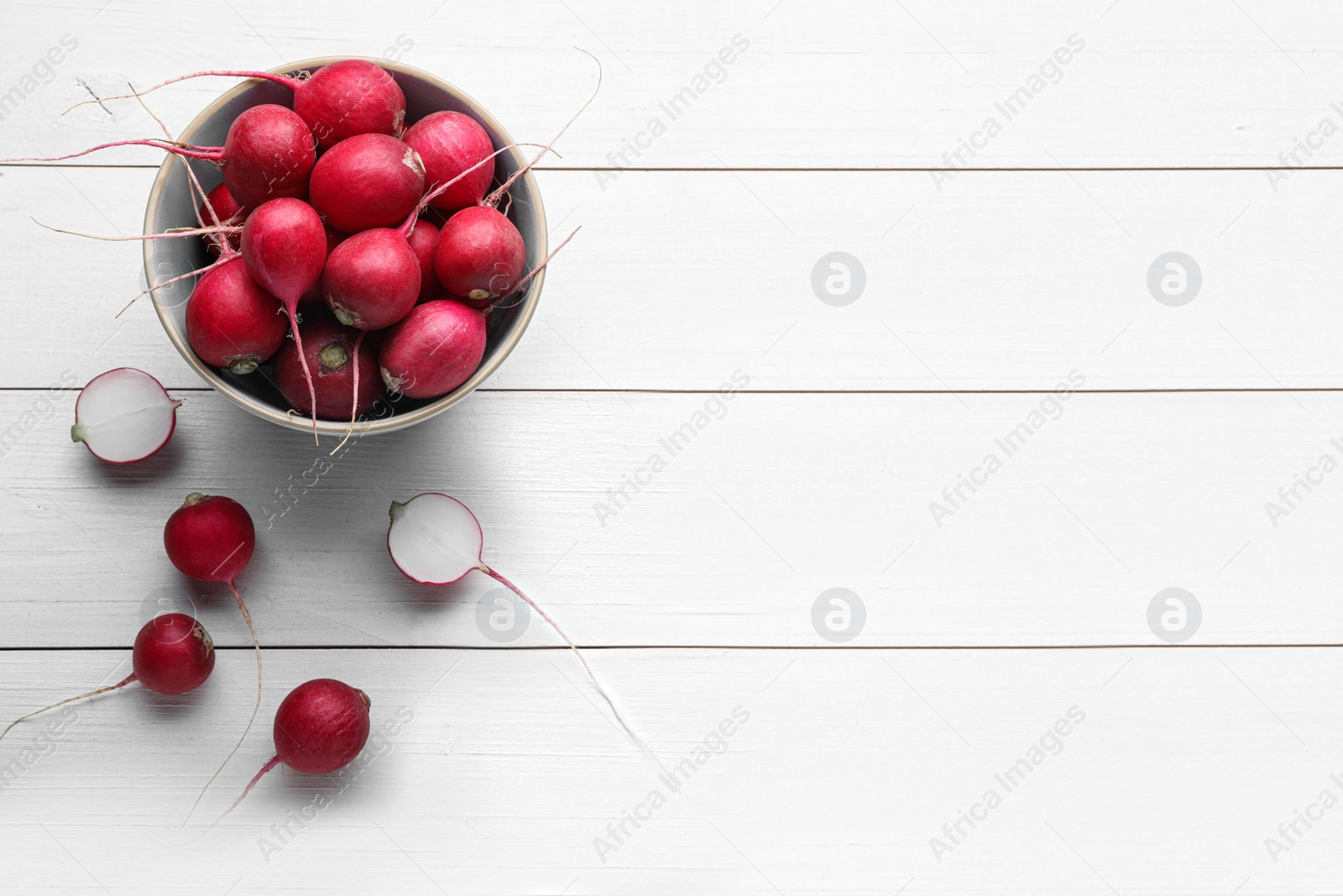 Photo of Bowl with fresh ripe radishes on white wooden table, flat lay. Space for text