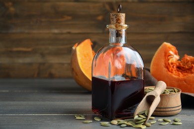 Glass bottle of oil with cut pumpkin and seeds on wooden table. Space for text
