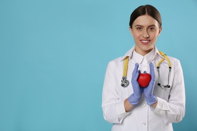 Photo of Doctor with stethoscope and red heart on light blue background, space for text. Cardiology concept