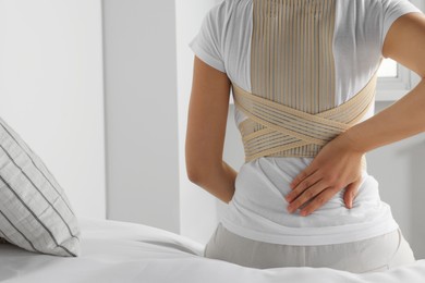 Woman with orthopedic corset sitting in bedroom, back view