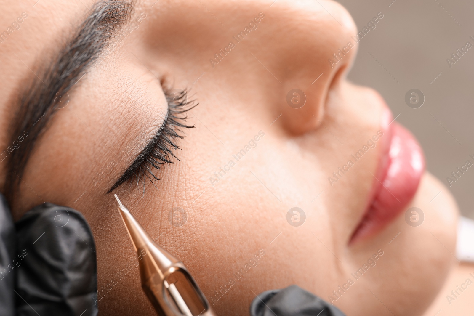 Photo of Young woman undergoing procedure of permanent eye makeup in tattoo salon, closeup