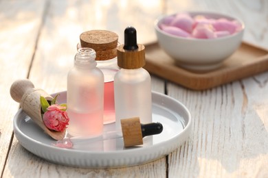Bottles of rose essential oil and flowers on white wooden table