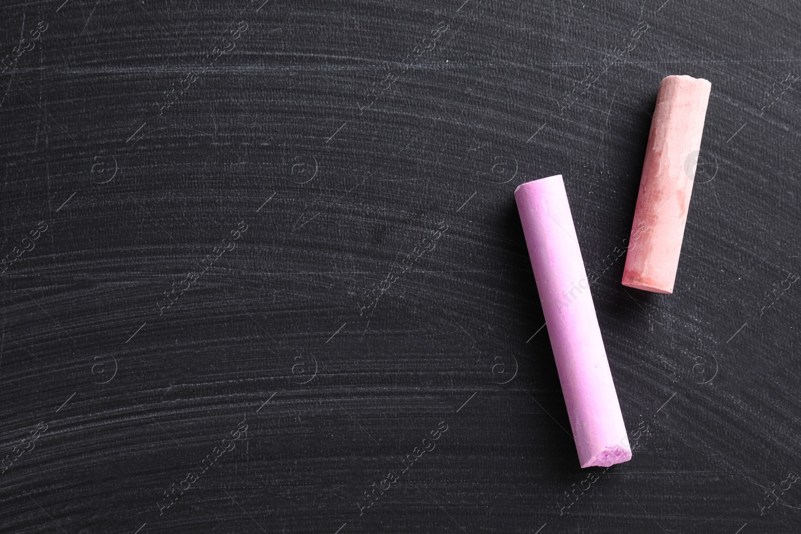 Photo of Pieces of color chalk on blackboard, flat lay. Space for text