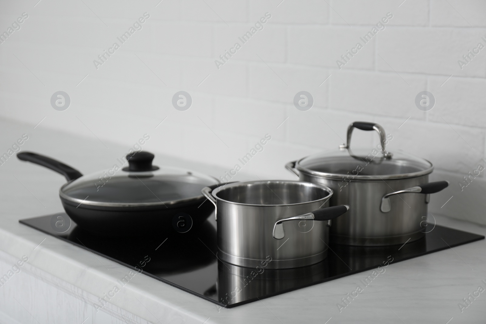 Photo of Saucepots and frying pan on induction stove in kitchen