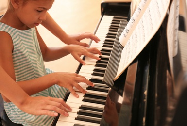 Photo of Young woman teaching little girl to play piano indoors