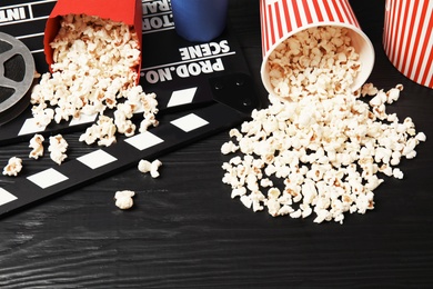 Photo of Tasty popcorn and clapperboard on wooden table. Cinema snack