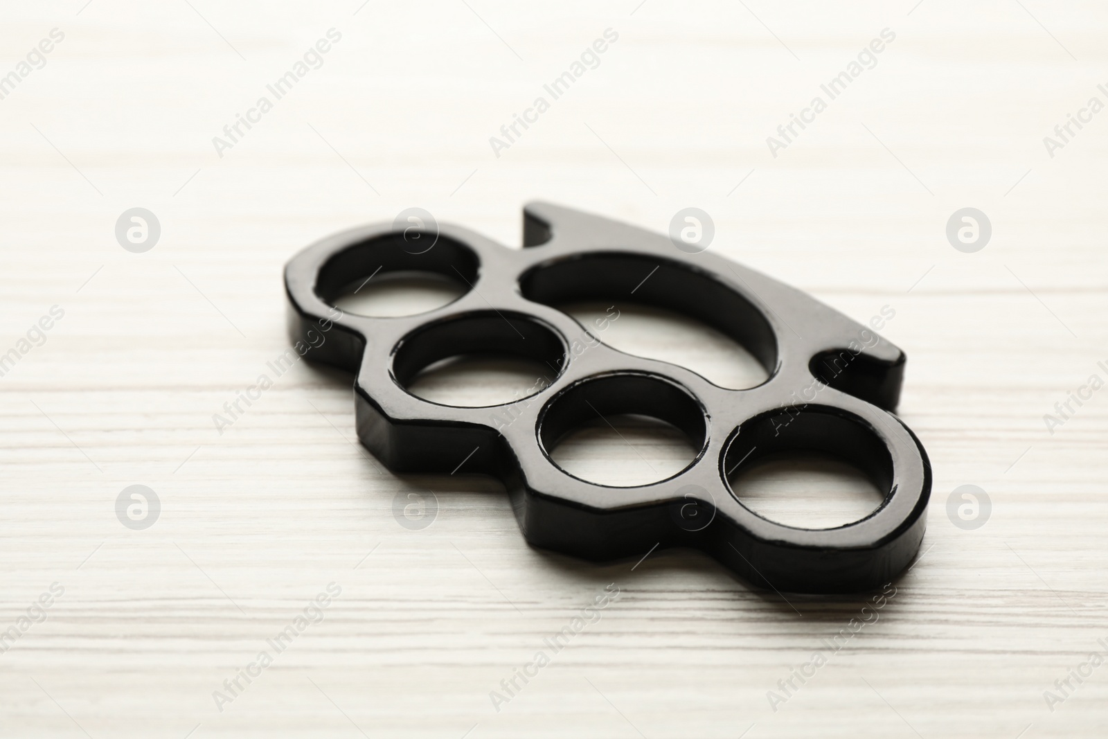 Photo of Black brass knuckles on white wooden background, closeup