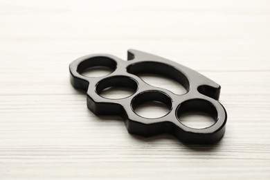 Photo of Black brass knuckles on white wooden background, closeup