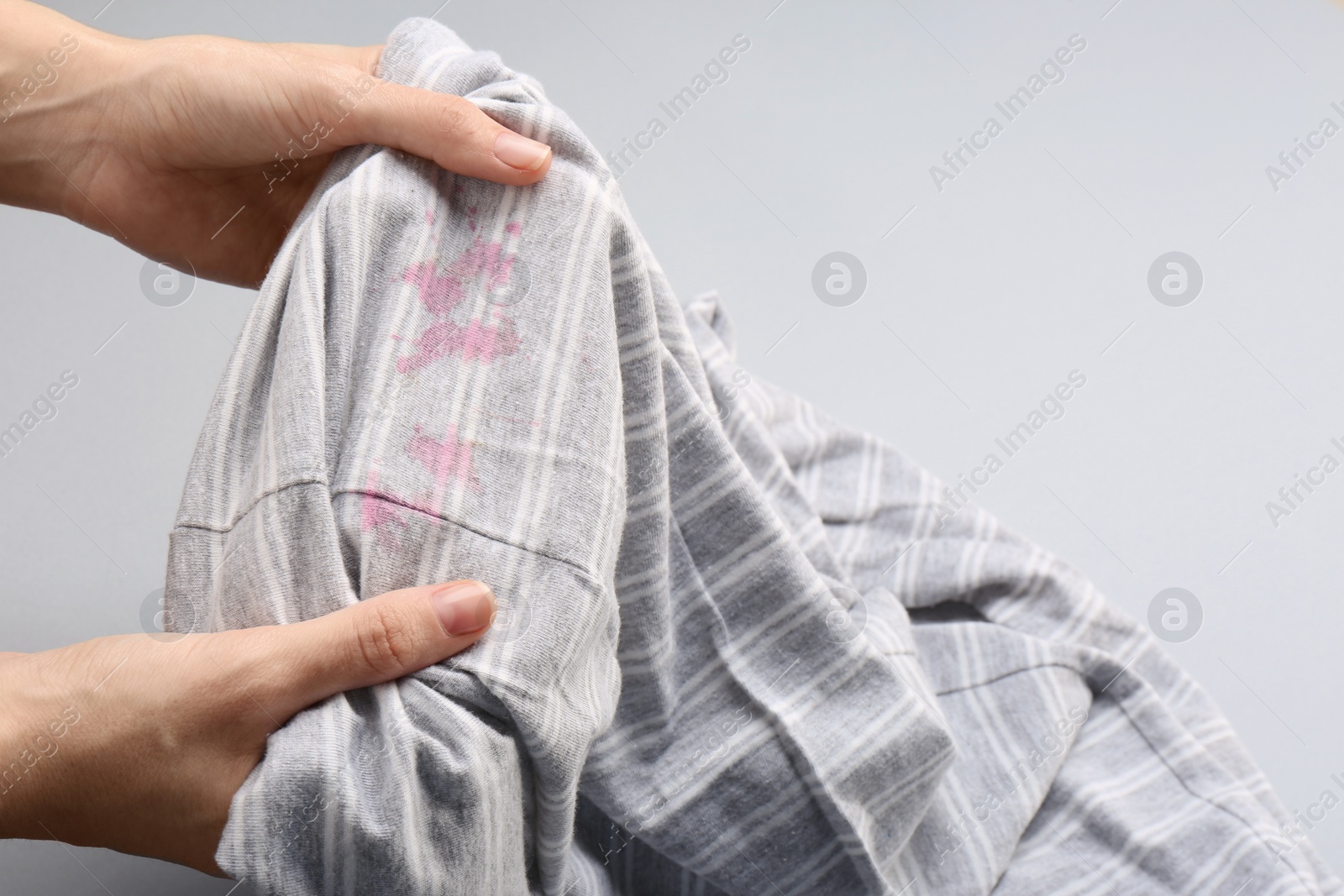 Photo of Woman holding striped shirt with stains on light grey background, closeup. Space for text