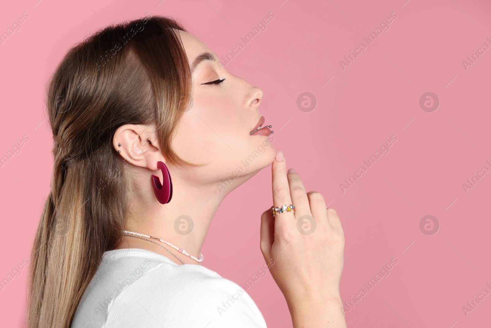 Photo of Young woman with lip and ear piercings on pink background. Space for text