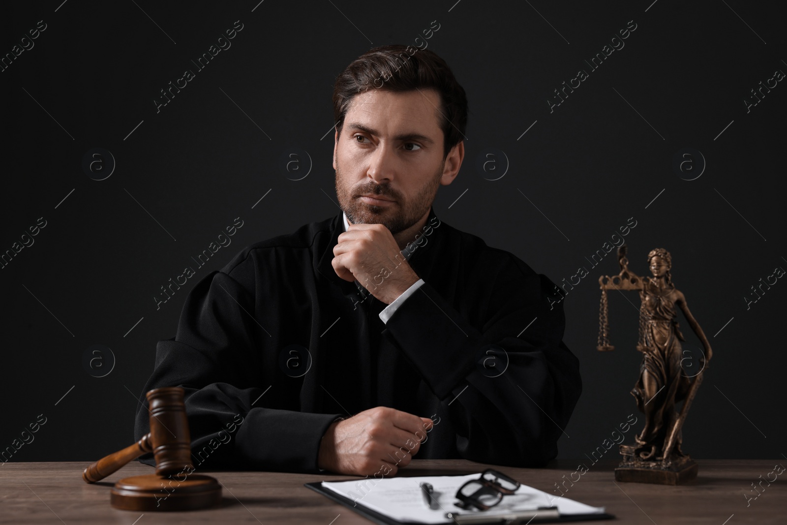 Photo of Judge with gavel and papers sitting at wooden table against black background