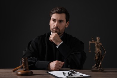 Judge with gavel and papers sitting at wooden table against black background