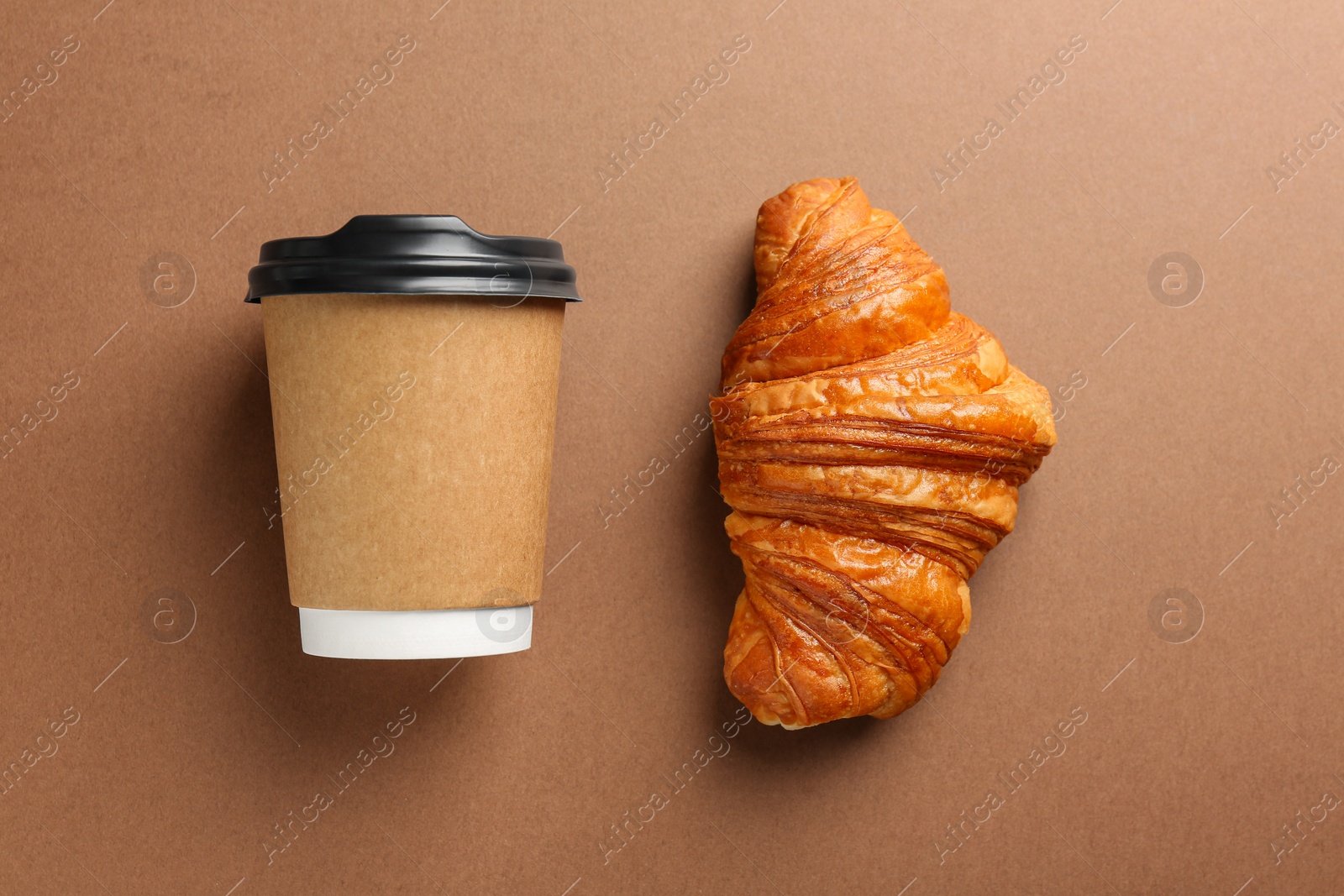 Photo of Delicious fresh croissant and paper cup with coffee on brown table, flat lay