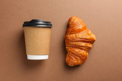 Delicious fresh croissant and paper cup with coffee on brown table, flat lay