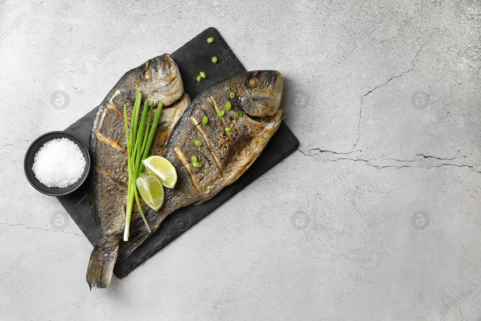 Photo of Seafood. Delicious baked fish served with green onion and lime on light textured table, top view. Space for text