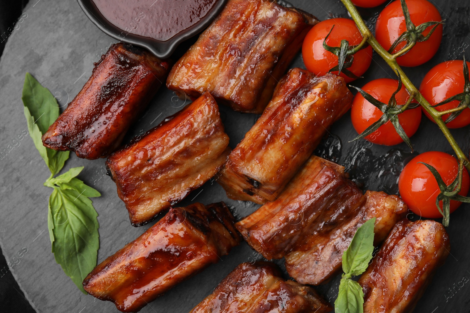 Photo of Tasty roasted pork ribs served with sauce, basil and tomatoes on table, top view