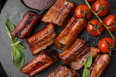 Photo of Tasty roasted pork ribs served with sauce, basil and tomatoes on table, top view