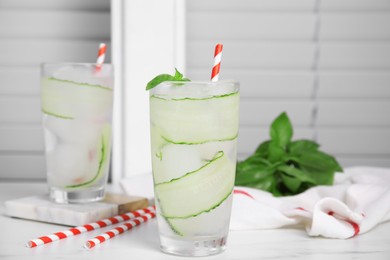 Glasses of refreshing cucumber water with basil on white table