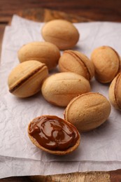Photo of Delicious nut shaped cookies with boiled condensed milk on parchment paper, closeup