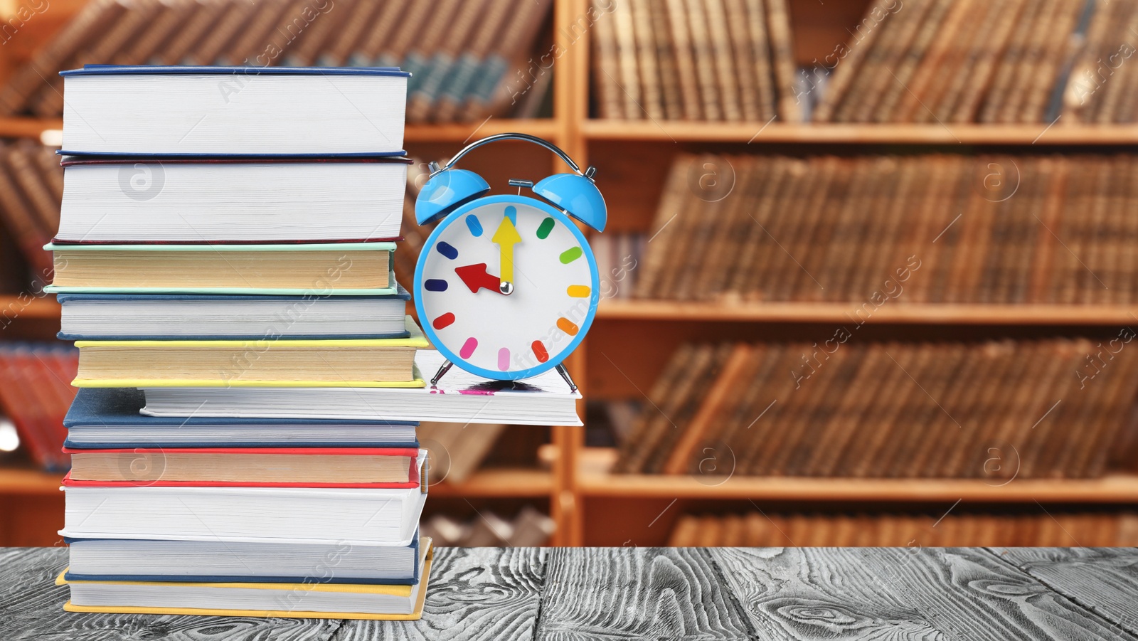 Image of Light blue alarm clock and different books on wooden table in library, space for text