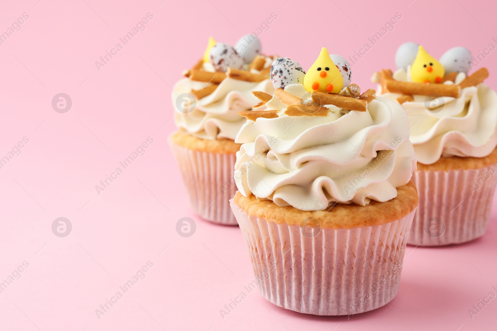 Photo of Tasty Easter cupcakes with vanilla cream on pink background, space for text